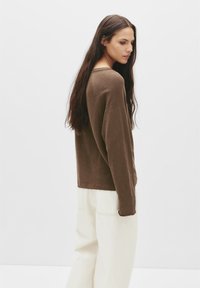 Brun langærmet skjorte i blødt stof med en afslappet pasform og rund halsudskæring, kombineret med løse hvide bukser.