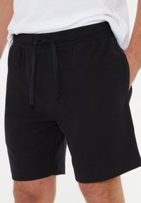 Svarta stickade shorts med elastisk midja, dragsko-stängning och sidofickor. Har en strukturerad tyg och avslappnad passform.