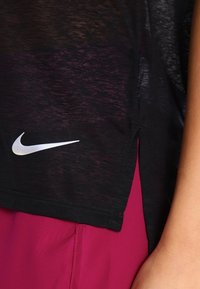 Czarna koszulka sportowa z fakturowanym wykończeniem, z wyraźnym białym logo Nike na dolnej stronie i luźnym krojem z bocznymi rozcięciami.