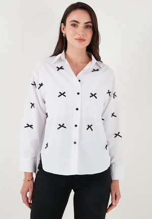 White button-up shirt with black cross embroidery, long sleeves, buttoned cuffs, and black buttons. Smooth texture, classic collar design.
