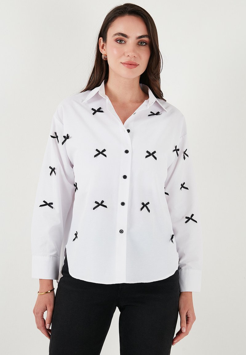 White button-up shirt with black cross embroidery, long sleeves, buttoned cuffs, and black buttons. Smooth texture, classic collar design.