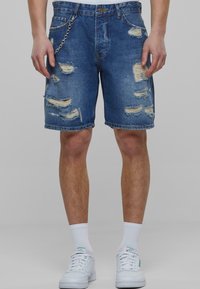 Shorts de mezclilla en azul medio con desgastes y bordes deshilachados. Presenta un detalle de cadena en el lateral y un diseño estándar de cinco bolsillos.