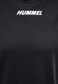Svart atletisk tröja gjord av texturerat tyg, med hög halsringning och framträdande vit "HUMMEL"-logotyp över bröstet.