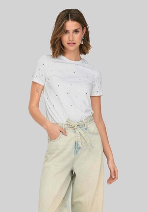 Camiseta blanca de manga corta con pequeños puntos negros, combinada con jeans de tiro alto de lavado claro con un cinturón atado.