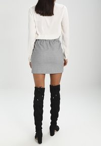 Bílá halenka s dlouhým rukávem, šedá mini sukně s houndstooth vzorem a elastickým pasem, a černé kozačky nad kolena na podpatku s krajkovými detaily.