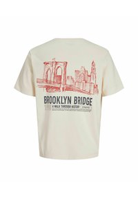 Beżowa koszulka z czerwonym szkicem mostu Brooklińskiego i panoramy miasta, z napisem „Brooklyn Bridge 1990 A Walk Through History” na plecach.
