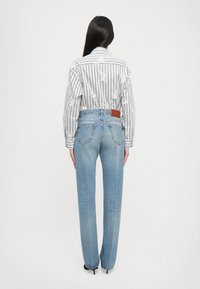 Ριγέ πουκά�μισο με μακριά μανίκια και λουλουδάτη κεντημένη διακόσμηση, σε συνδυασμό με ανοιχτό μπλε ψηλόμεσες τζιν παντελόνες, που περιέχουν δερμάτινη ετικέτα στο πίσω μέρος.