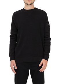 Maglione nero lavorato a maglia con collo rotondo, orlo e polsini a coste, e una patch con logo sulla manica sinistra. Design in tessuto strutturato.