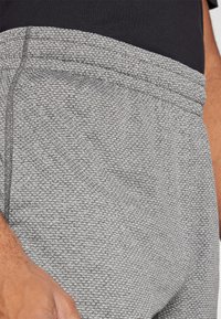Grau strukturierte Jogginghosen mit elastischem Bund und sichtbaren Nähten. Der Stoff hat ein gewebtes Muster, das ein sportliches Erscheinungsbild vermittelt.