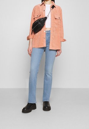 Korálová kordurová košile, bílý cropped top, světle modré džíny a černé platformové boty. Černá kabelka přes rameno se stříbrným řetízkem.