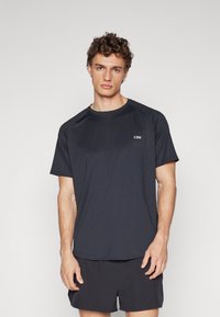 Camiseta deportiva oscura de manga corta, con cuello redondo y fabricada en tejido transpirable. Pequeño logo en el lado izquierdo del pecho. Color negro atemporal.