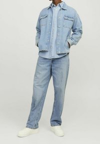 Ljusblå denimjacka med två bröstfickor, ihop med en ljusblå skjorta med knappar och ljusblå löst sittande jeans, kompletterat med vita sneakers.