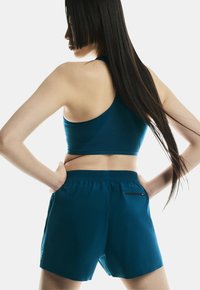 Teal sportbeha met een geribbelde textuur, gecombineerd met bijpassende teal shorts met een elastische tailleband en een ritsachterzak.