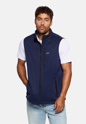 Chaleco de forro polar azul marino con cuello alto, cremallera frontal y bolsillos laterales. Cuenta con un parche de logo en el pecho. Textura suave.