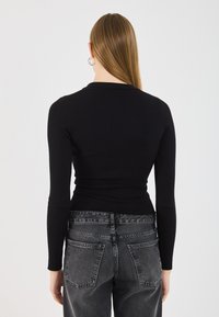 Black ribbed long-sleeve top with a fitted silhouette, paired with dark gray high-waisted jeans featuring a classic pocket design.