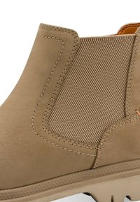 Bottine beige avec panneau élastique texturé sur les côtés, couture détaillée et semelle robuste conçue pour une utilisation en extérieur.