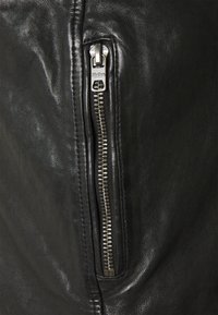 Svart läderjacka med en silverfärgad metalldragkedja på sidan, med en slät textur och en figursydd design. Synlig accentuerad sömnad.