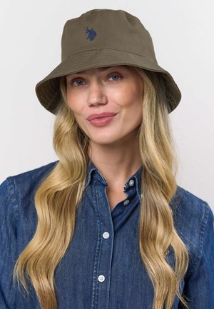 Olivovo zelený klobúk v tvare vedra vyrobený z látky s jemnou textúrou. Má vyšitý emblém v námorníckej modrej farbe. Široký okraj a voľný strih.