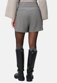 Shorts med houndstooth-mönster och hög midja, med två bakfickor, i kombination med knähöga svarta gummistövlar och grå strumpor.