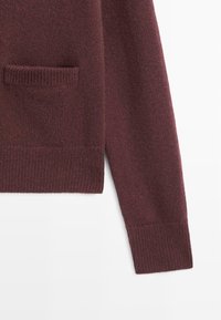 Maroon knitted sweater featuring a ribbed texture, single front pocket, and ribbed cuffs. Smooth finish and soft fabric.