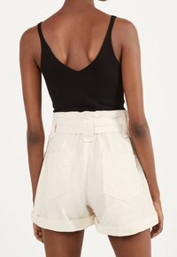 Musta ribbineulottu toppi, jossa on V-mallinen selkä, yhdistetty vaalean beigeihin vyötäröhiusriteisiin käännetyin lahkeensuin ja vyötärön nyörityksellä varustettuihin korkeavyötäröisiin shortseihin.