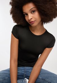 T-shirt nera aderente con maniche corte, realizzata in materiale liscio. Indossata con jeans di denim azzurro chiaro, caratterizzati da una vestibilità comoda e una texture scolorita.