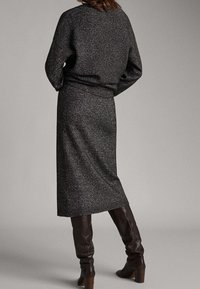 Langer grauer Strickpullover mit rundem Ausschnitt, kombiniert mit einem passenden grauen Rock. Das Outfit besticht durch ein strukturiertes Muster und dunkelbraune kniehohe Stiefel.
