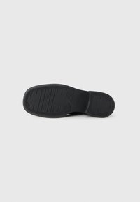 Black shoe sole with a patterned tread for grip. Material appears rubberized, featuring a flat design and rounded shape. No visible branding.