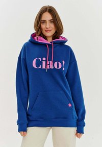 Modrá mikina s kapucí a růžovými detaily, na přední straně s velkým nápisem "Ciao!". Vyrobena z měkkého materiálu, má přední kapsu a stahovací kapuci.