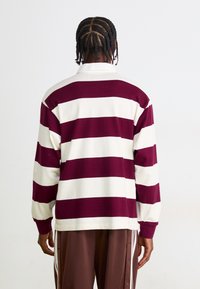 Hosszúujjú polo póló váltakozó bordó és fehér csíkokkal, pamutból készült, klasszikus gallérral és laza szabással.