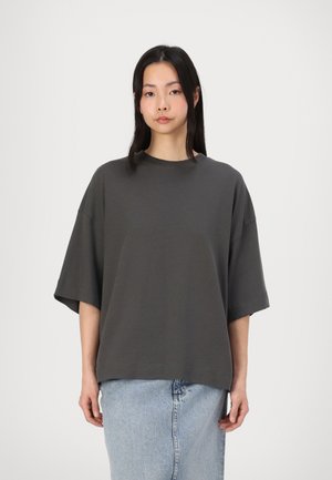 Dunkelgraues, übergroßes T-Shirt mit kurzen, weiten Ärmeln und rundem Halsausschnitt. Weiche, glatte Textur, kombiniert mit einem leichten Jeansrock.