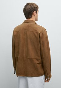 Braune Wildlederjacke mit Kragen, Rückenpasse und knöpfbaren Manschetten, von hinten vor einem neutralen Hintergrund präsentiert.
