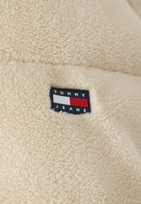 Tissu polaire beige doux avec un petit patch rectangulaire du logo Tommy Jeans en bleu marine, blanc et rouge cousu sur la surface.