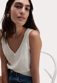 Vit stickad linne med V-ringning, försedd med glittrande detaljer, tillsammans med avslappnade denimshorts. Slät textur, avslappnad passform.