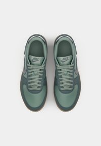 Green Nike sneakers with a mix of matte and glossy textures, featuring a rounded toe, flat laces, and a gum sole.