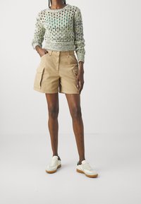 Sweter dziany w zielonych i kremowych odcieniach, połączony z khaki szortami pojemnymi. Białe trampki z zielonymi i brązowymi akcentami dopełniają stylizację.