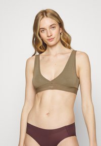 Bralette castanho, sem costuras, com alças largas e um design de decote V profundo. Textura macia com um detalhe de logo sob o busto.