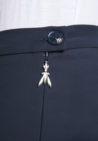 Marineblauwe broek met ritssluiting, voorzien van een zilverkleurige hardwareaccent en een zwarte knop in de taille, gemaakt van een gladde stof.