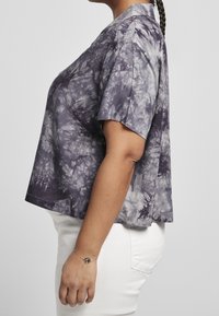 T-shirt viola con tie-dye, maniche corte, vestibilità comoda e scollatura rotonda, realizzato in tessuto morbido. Indossato con pantaloni bianchi.