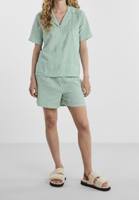 Zielono-biała piżama w paski składająca się z krótkiego, zapinanego na guziki podkoszulka oraz pasujących szortów, wykonana z lekkiego materiału, w zestawie z puszystymi klapkami.
