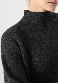 Sweater de gola alta cinza-escuro com um padrão de malha texturizado. Apresenta um corte descontraído e um material macio e grosso, enfatizando o calor e o conforto.