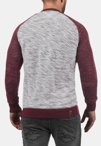 Maglione color bordeaux e grigio con tessuto testurizzato e maniche raglan. Polsini e orlo a coste, con un piccolo etichetta del marchio in vita.
