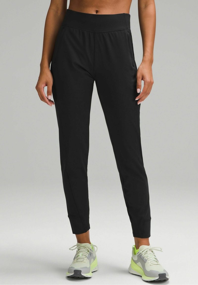 Svarta sportiga joggers med en åtsittande, hög midja, som har en slät yta och ribbade ankle cuffs. I kombination med ljusgröna sneakers.