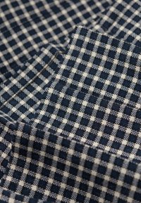 Bomuldsstof med et mønstret væv, der har et navy og cremet ternet design, der fremhæver små pilmotiver i en struktureret finish.