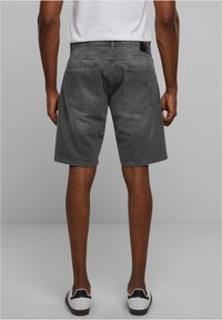 Shorts de denim gris con corte recto, que cuentan con dos bolsillos traseros y un ligero desgaste. Combinados con zapatillas blancas, vistos desde la parte trasera.