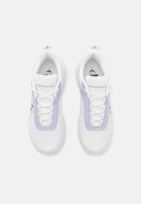 Baskets de sport blanches et lavande présentant un dessus texturé, un système de laçage et un logo sur la languette, avec une semelle extérieure flexible.