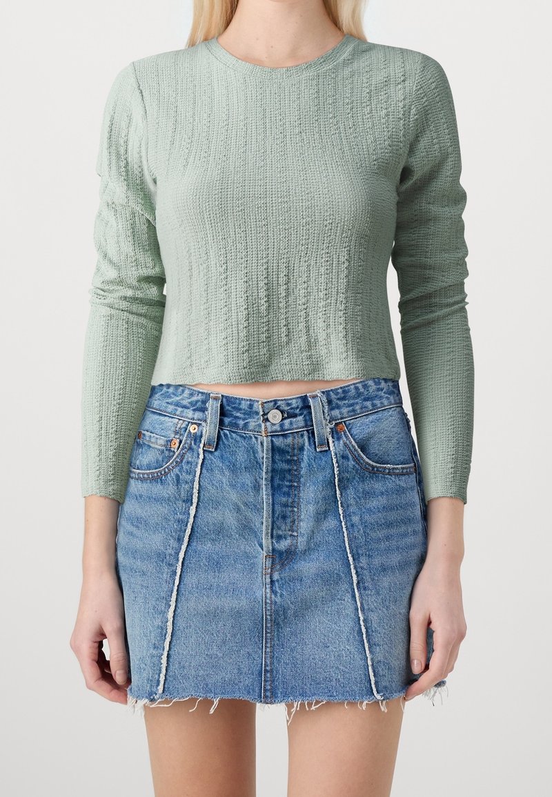 Hellgrünes, strukturiertes Longsleeve-Oberteil mit einem cropped Schnitt, kombiniert mit einem blauen Denim-Minirock mit Fransen und vorderen Nähten.