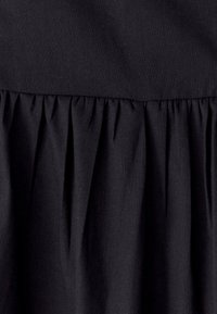 Črn material z nabranim detajlom, ki prikazuje gladko teksturo in strukturirano obliko. Naborki ustvarjajo subtilen, tekoč učinek.