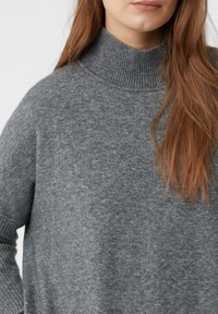 Grau gestrickter Rollkragenpullover mit lockerer Passform. Merkmale eine gerippte Textur am Kragen und an den Bündchen, die ein sanftes, warmes Aussehen zur Geltung bringt.