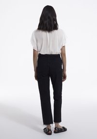 Svarta högmidjade jeans med fransad nederkant, ihopparat med en genomskinlig vit blus. Outfiten fullbordas med svarta sandaler med silverdetaljer.